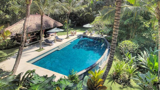 A swimming pool surrounded by palm trees and tropical plants, with a thatched-roof structure and lounge chairs. - Luxury Hillside Retreat with Private Pool – Bali Villa 1049 (Bali)