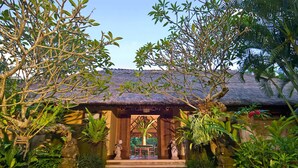 A traditional thatched-roof structure with a stone entrance, surrounded by lush greenery and tropical plants. - Luxury Hillside Retreat with Private Pool – Bali Villa 1049 (Bali)