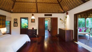 A bedroom with a large bed, wooden dresser, and a desk with a vase. There are framed pictures on the wall and a window with a view of greenery. - Luxury Hillside Retreat with Private Pool – Bali Villa 1049 (Bali)