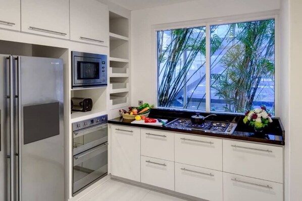A modern kitchen with white cabinets, a built-in oven, a microwave, and a gas stove.