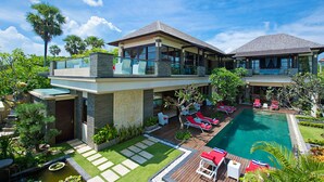 Una casa moderna de dos pisos con una gran piscina, mobiliario exterior y un paisaje exuberante.