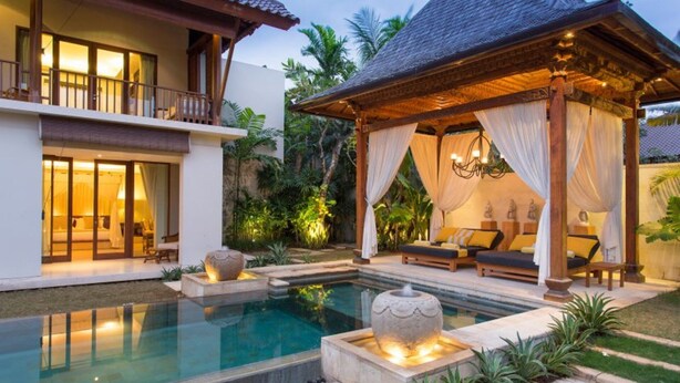 Um resort com piscina, área de estar coberta com almofadas e um jardim bem cuidado.