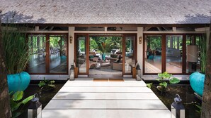 A modern building with large glass doors leading to a spacious interior with a central seating area and a view of lush greenery outside. - 5 Star Villa in Bali, Minutes from the Beach, Bali Villa 1026 (Bali)