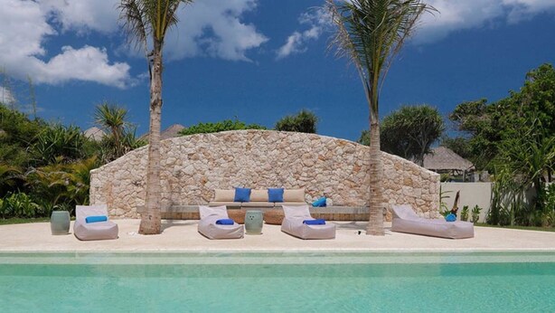 Un salon de bord de piscine avec des murs en pierre et de nombreux fauteuils confortables.