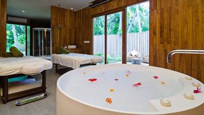 Une salle de spa équipée de deux tables de massage, d’une grande baignoire avec des bougies et offrant une vue sur l’extérieur.
