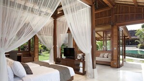A bedroom with a large bed, a TV, and a view of a swimming pool. - Secluded Comfort, Steps from the Beach – Bali Villa 1096 (Bali)