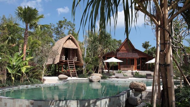 A pool area with a thatched-roof hut and a wooden building, surrounded by tropical vegetation. - Secluded Comfort, Steps from the Beach – Bali Villa 1096 (Bali)
