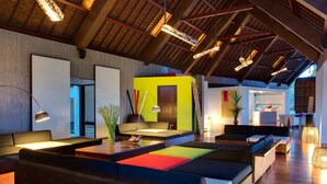 A modern hotel lobby with a high ceiling, exposed beams, and a mix of seating areas including sofas and a long communal table. - Ocean View Luxury Escape Lombok Villa 1133 (Lombok)