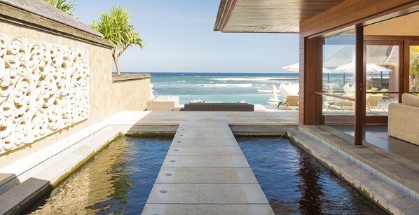 A pool with a view of the ocean, a stone wall with carvings, and a seating area with umbrellas.