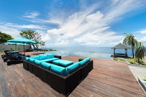 Eine Holzterrasse mit Pool, Liegestühlen und einem Pavillon mit Blick auf ein Gewässer.