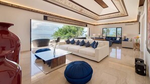 Ein geräumiger Wohnbereich mit großem Fenster, einem weißen Sofa mit blauen Kissen, einem blauen Hocker und einer roten Vase.