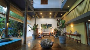 Zona interior espaiosa amb zona de seients central, plantes grans en testos i ventilador de sostre.