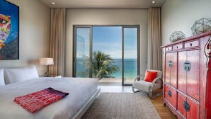 A hotel room with a large bed, a red cabinet, a chair, and a view of the ocean.
