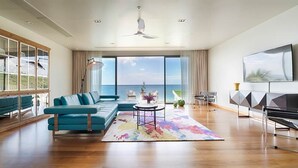 A spacious living room with a large sofa, a coffee table, and a view of the sea through large windows.