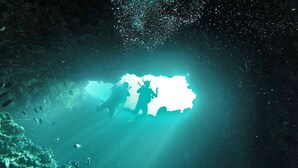 Une grotte dont le fond est illuminé par une source de lumière vive, et qui est entourée d’eau et de poissons.