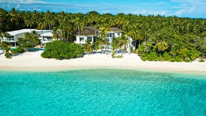 Une propriété située en bord de mer, comprenant plusieurs maisons, une plage de sable et une mer turquoise aux eaux cristallines.