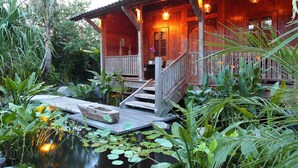 Ein hölzernes Haus mit Veranda, umgeben von üppigem Grün und einem Teich.