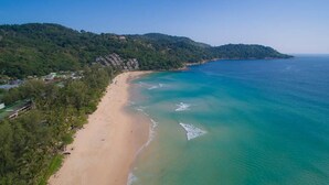 Eine Küstenlandschaft mit Sandstrand, blauem Meer und bewaldetem Hang.