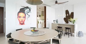 Un espace repas moderne avec une table ronde, des chaises, un grand saladier à fruits placé au centre et une grande œuvre d’art abstraite accrochée au mur.