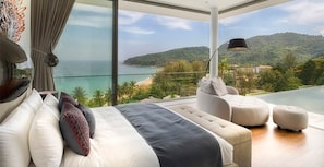 A bedroom with a large bed, a sofa, and a view of the sea and hills.