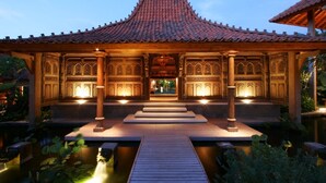 A traditional building with a tiled roof, ornate wooden doors, and a wooden deck leading to a pond. - Seminyak’s Hidden Gem of Grace, Bali Villa 1101 (Bali)