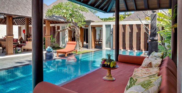 A pool area with a lounge chair, a table with fruit, and a covered seating area. - Serene luxury in lush gardens, Bali Villa 1124 (Bali)