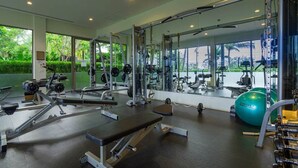 Un gimnasio con diversos equipos de ejercicio, amplias ventanas y vistas a zonas verdes.