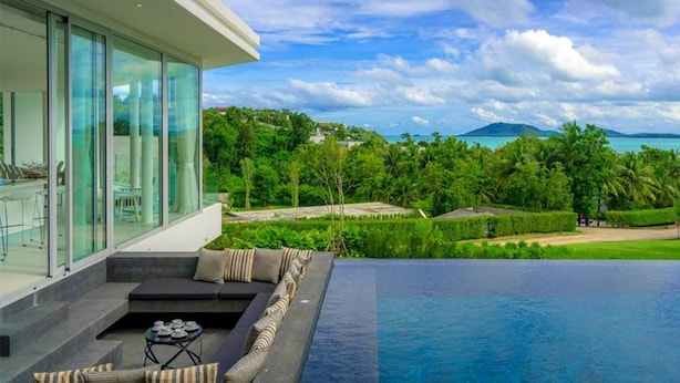 Una casa moderna con fachada de vidrio, piscina y vistas al mar y la vegetación.