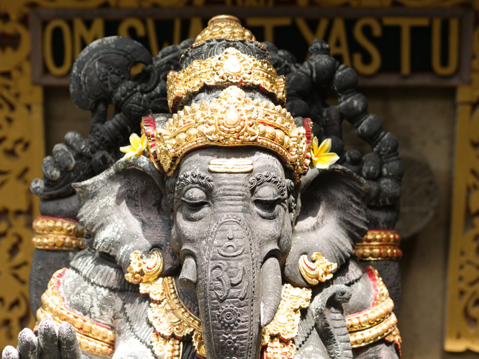A detailed statue of an elephant with intricate golden decorations and a sign in the background.