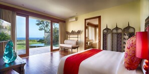 A bedroom with a large bed, a view of the ocean, a balcony, and a traditional-style chair.