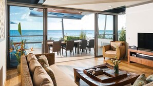 A modern living room with a large sliding glass door leading to a balcony with a view of the ocean. There is a sofa, a coffee table, and a TV stand with a flat-screen TV. - Luxury Family Retreat with Private Chef, Koh Samui Villa 1001 (Koh Samui)