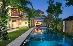 Una casa moderna de dos pisos con piscina, abundante vegetación e interior bien iluminado.