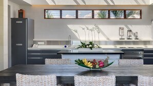 Una cocina moderna con una isla central, una mesa de comedor con sillas tejidas y un arreglo decorativo de orquídeas.