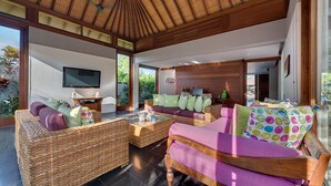 Una sala de estar moderna con muebles de mimbre, un televisor de pantalla plana y un ventanal con vistas al verdor.