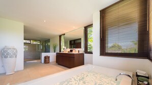 Une salle de bain moderne avec une grande baignoire, un meuble-lavabo avec un miroir et une fenêtre équipée de stores.
