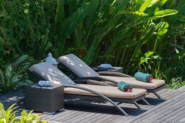 A row of three wicker lounge chairs with cushions, arranged on a wooden deck.