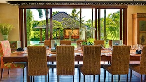 Un coin repas avec une grande table et des chaises en osier, une plante en pot et une vue sur un paysage tropical.