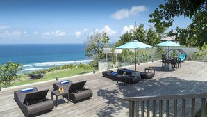 Eine Terrasse mit Gartenmöbeln, einem Tisch und zwei Sonnenschirmen mit Blick auf den Ozean.