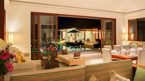 Ein modernes Wohnzimmer mit Pool, einer Couch, einem Esstisch und Blick auf den Poolbereich.