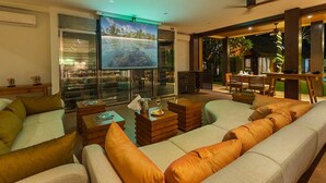Una sala de estar moderna con un sofá grande, una mesa de centro y una pantalla de televisión que muestra una escena de playa tropical.