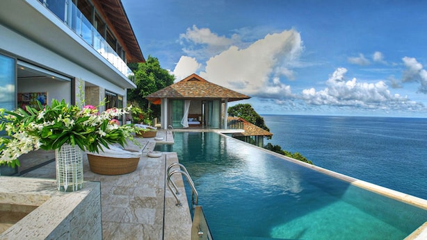 Une piscine à débordement luxueuse offrant une vue dégagée sur l’océan, un pavillon privé et un jardin bien entretenu.