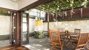 An outdoor patio with a wooden table and chairs, a statue, and a stone wall.