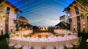 An outdoor wedding reception with round tables, white chairs, and string lights. - Rent a Luxury Villa in Bali Close to the Beach, Bali Villa 1130 (Bali)