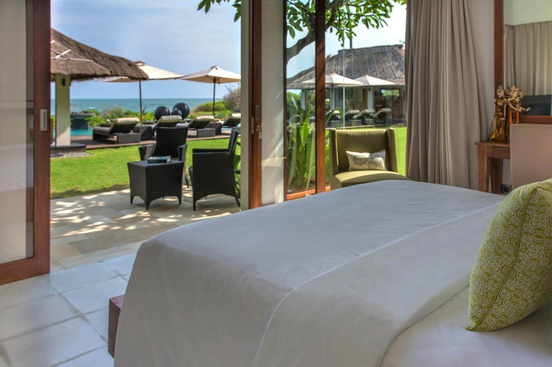 Une chambre avec un grand lit, une vue sur l’océan et un espace extérieur aménagé avec des parasols.