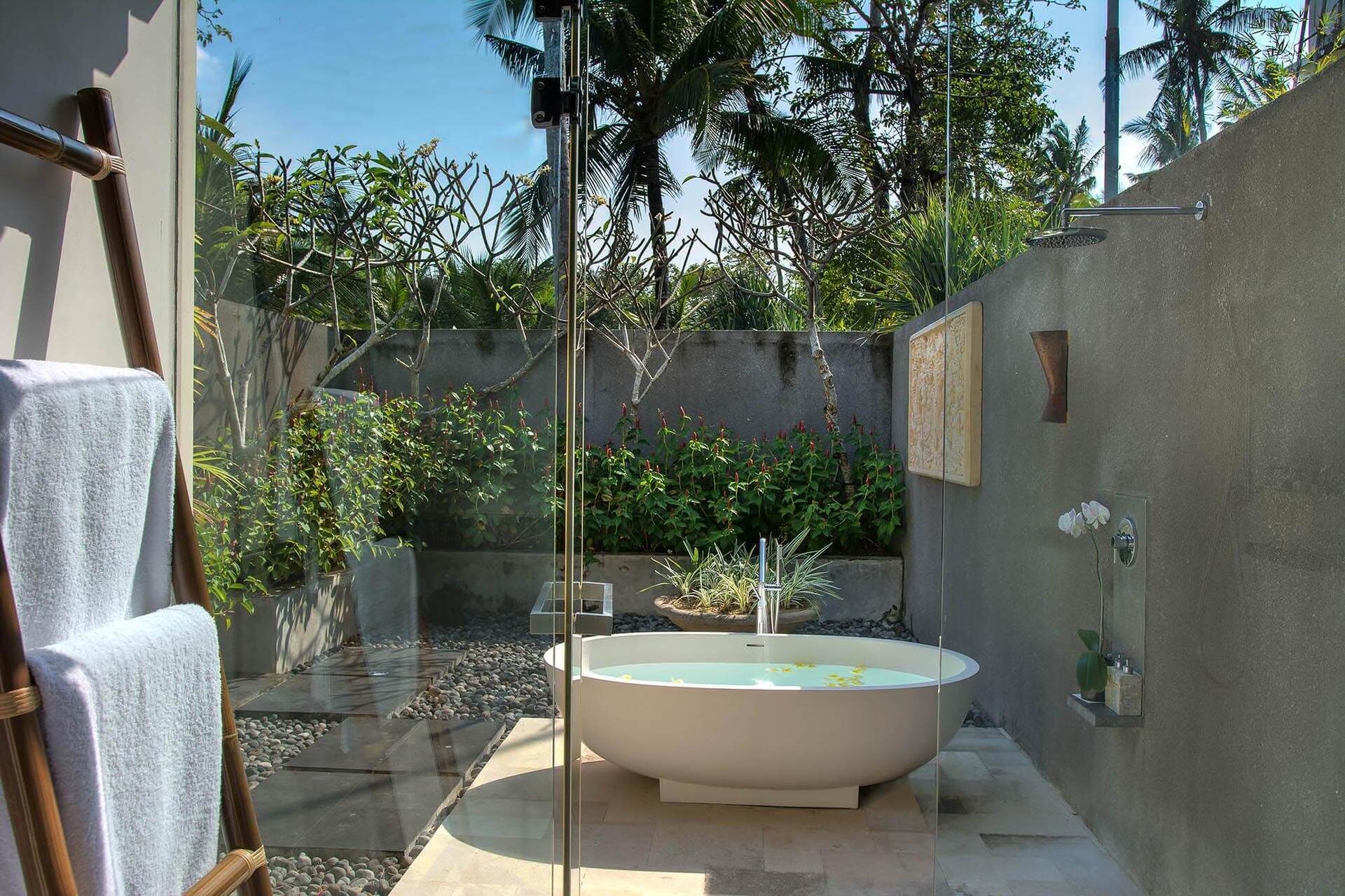 Ein Wellnessbereich mit einer freistehenden Badewanne, einem Bambus-Sessel und einer Duschkabine aus Glas.