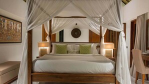 A four-poster bed with white linens, a wooden headboard, and a canopy. There are two bedside lamps, a wall-mounted clock, and a cushioned bench to the left. - Rent a Luxury Villa in Bali Close to the Beach, Bali Villa 1130 (Bali)