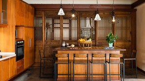 A kitchen with wooden cabinets, a central island with chairs, hanging pendant lights, and a potted plant. - This Perfect 5 Star Villa in Koh Samui with Beachside Private Pool, Villa Waimarie 1005 (Koh Samui)