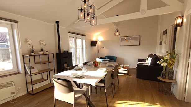 Un salon moderne avec un coin repas, doté d’un parquet, d’une cheminée et d’un canapé noir.