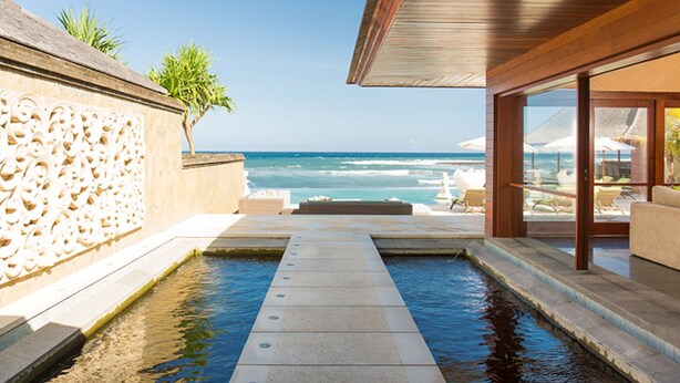 A pool area with a view of the ocean, a palm tree, and outdoor seating.