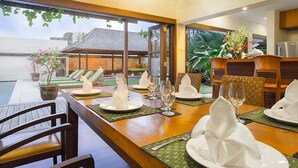 A dining area with a view of a pool and a thatched-roof building.